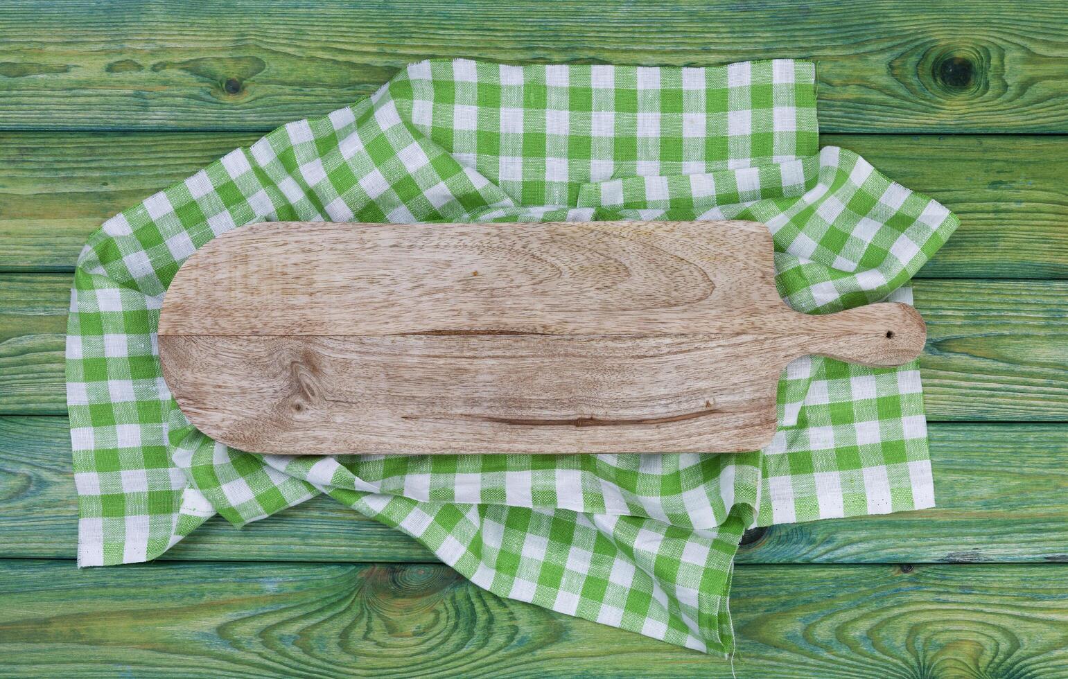 Cutting board on green checkered tablecloth, top view photo