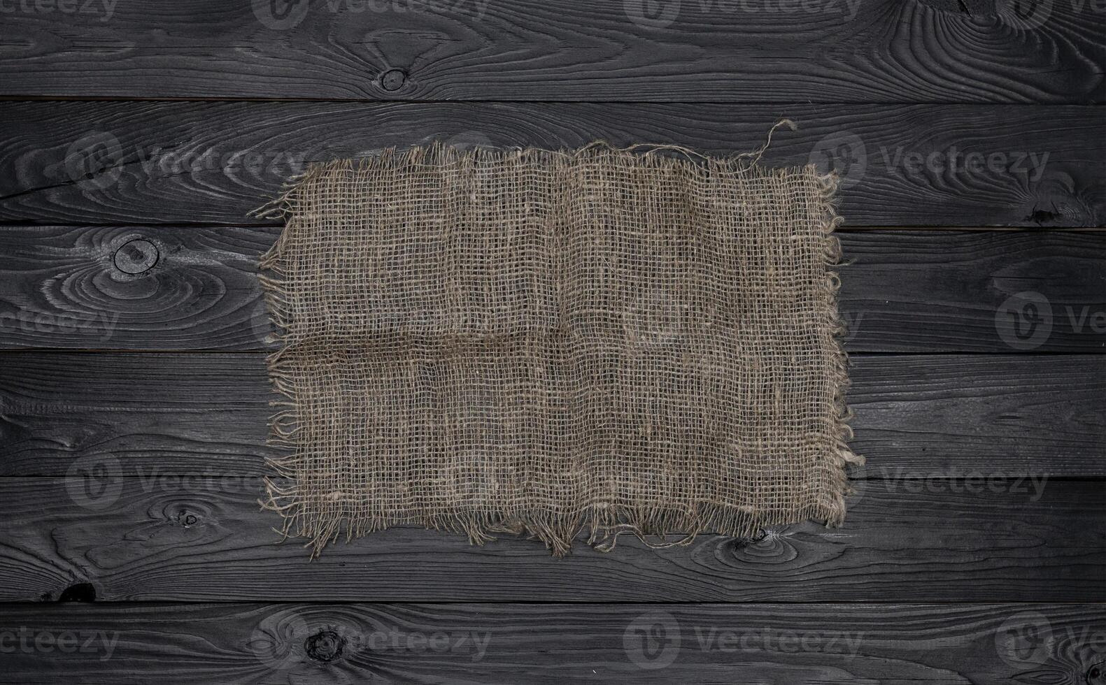 Old burlap fabric napkin on black wooden background, top view photo