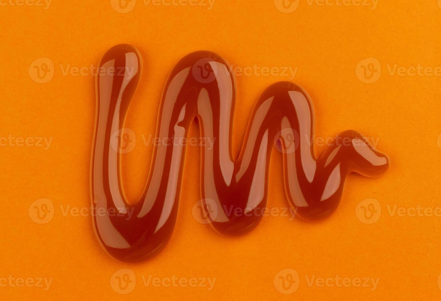 Caramel sauce on orange color background, top view photo