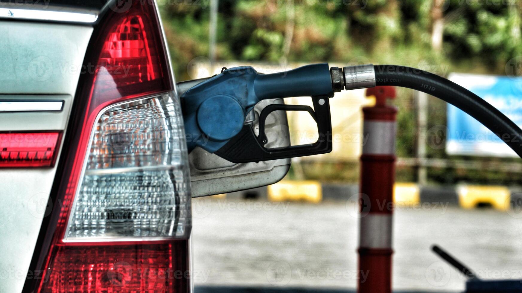 A white car is filling its gas tank at a gas station. The nozzle is blue. photo