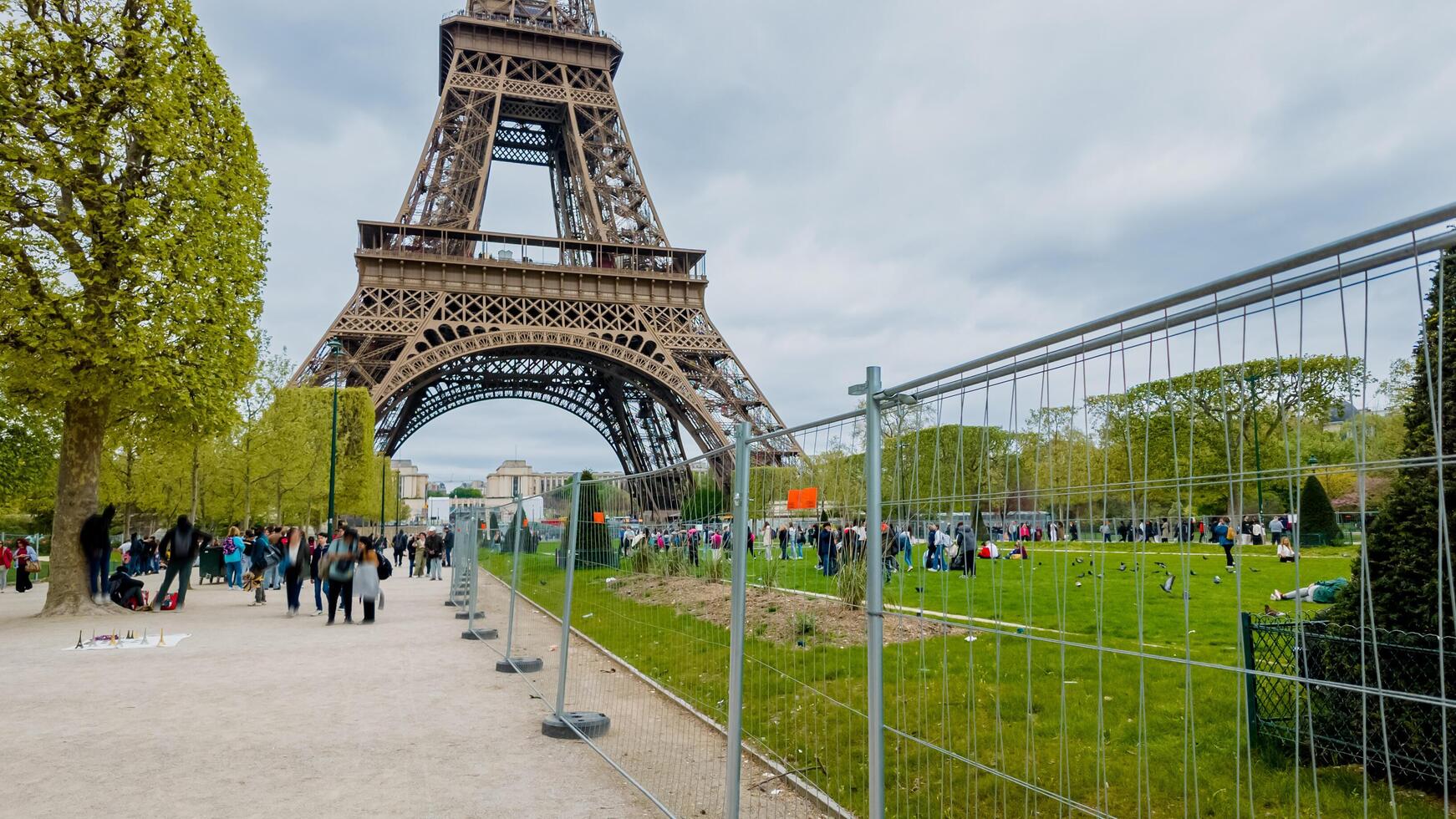 Tourists and locals enjoy a spring day near the Eiffel Tower in Paris, France, with security fencing in place, on April 14th, 2024, perfect for travel and European culture themes photo