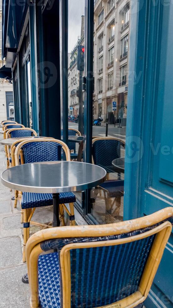 Empty blue wicker chairs at a Parisian sidewalk cafe with a reflective metal table, evoking concepts of travel, European culture, and leisure photo