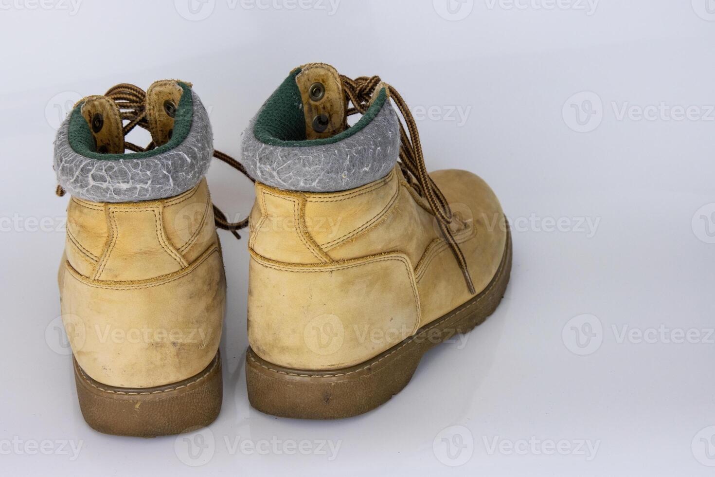 Pair of worn old yellow hiking trekking lace boots Isolated on white glossy surface with beautiful reflection effect. Second hand tourist walking shoes. Back view. Copy Space. White background. photo