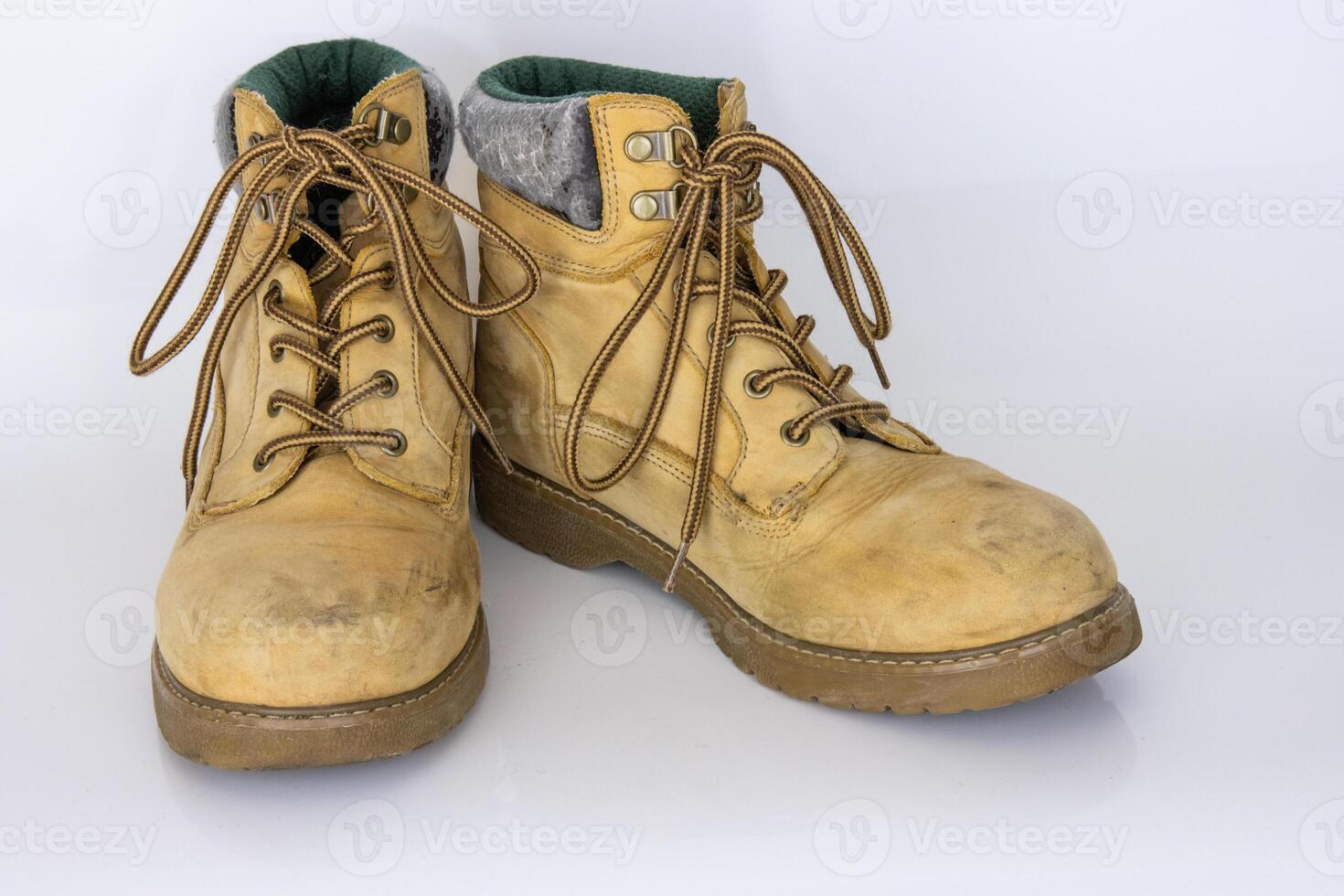 Pair of worn old yellow hiking trekking lace boots Isolated on white glossy surface with beautiful reflection effect. Second hand tourist walking shoes. Side view. Copy Space. White background. photo