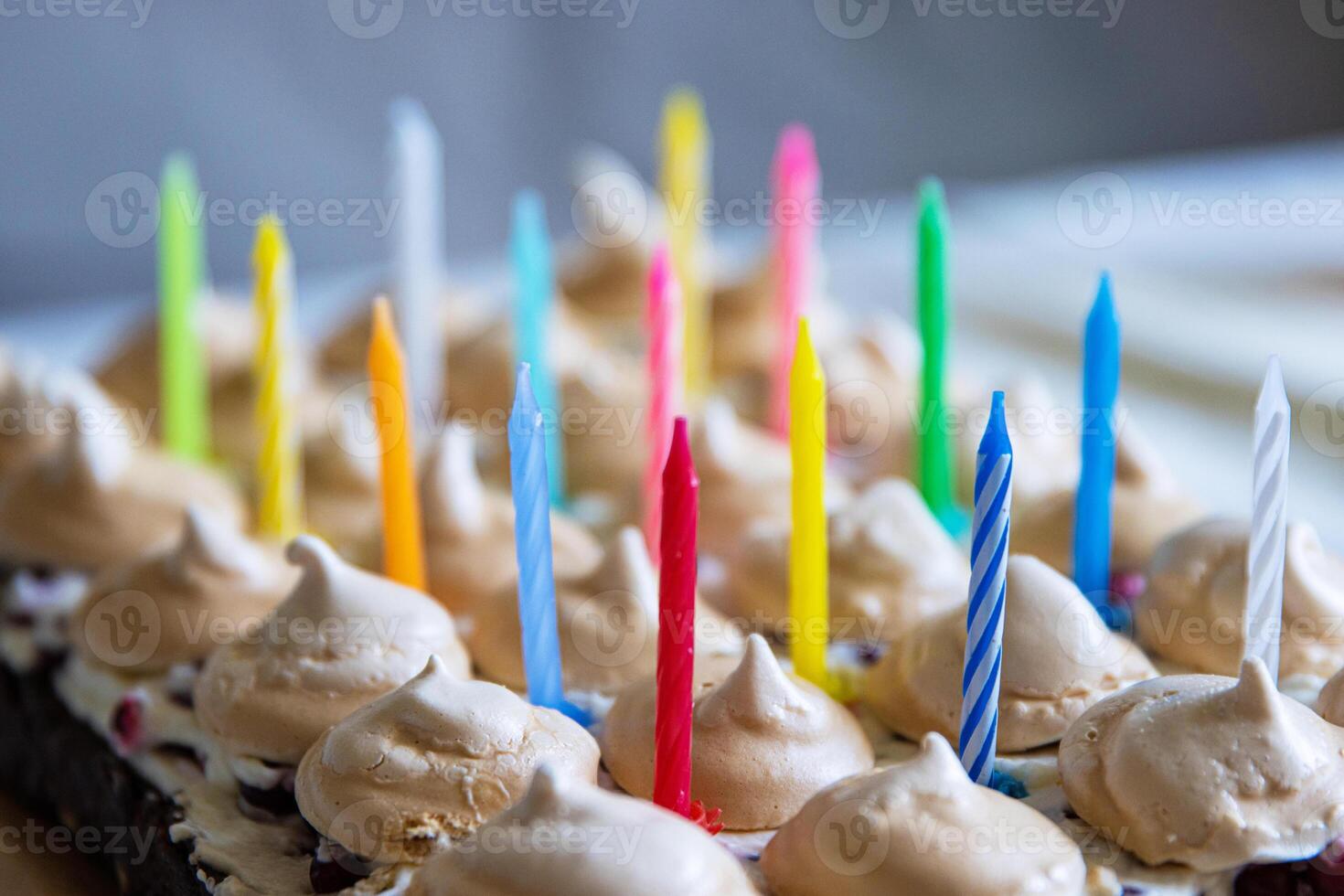 Birthday cake with white whipped cream, meringues and cranberries, decorated with multicolored lit candles. Happy Birthday concept. Tradition of making a wish blowing out candles. Selective focus. photo