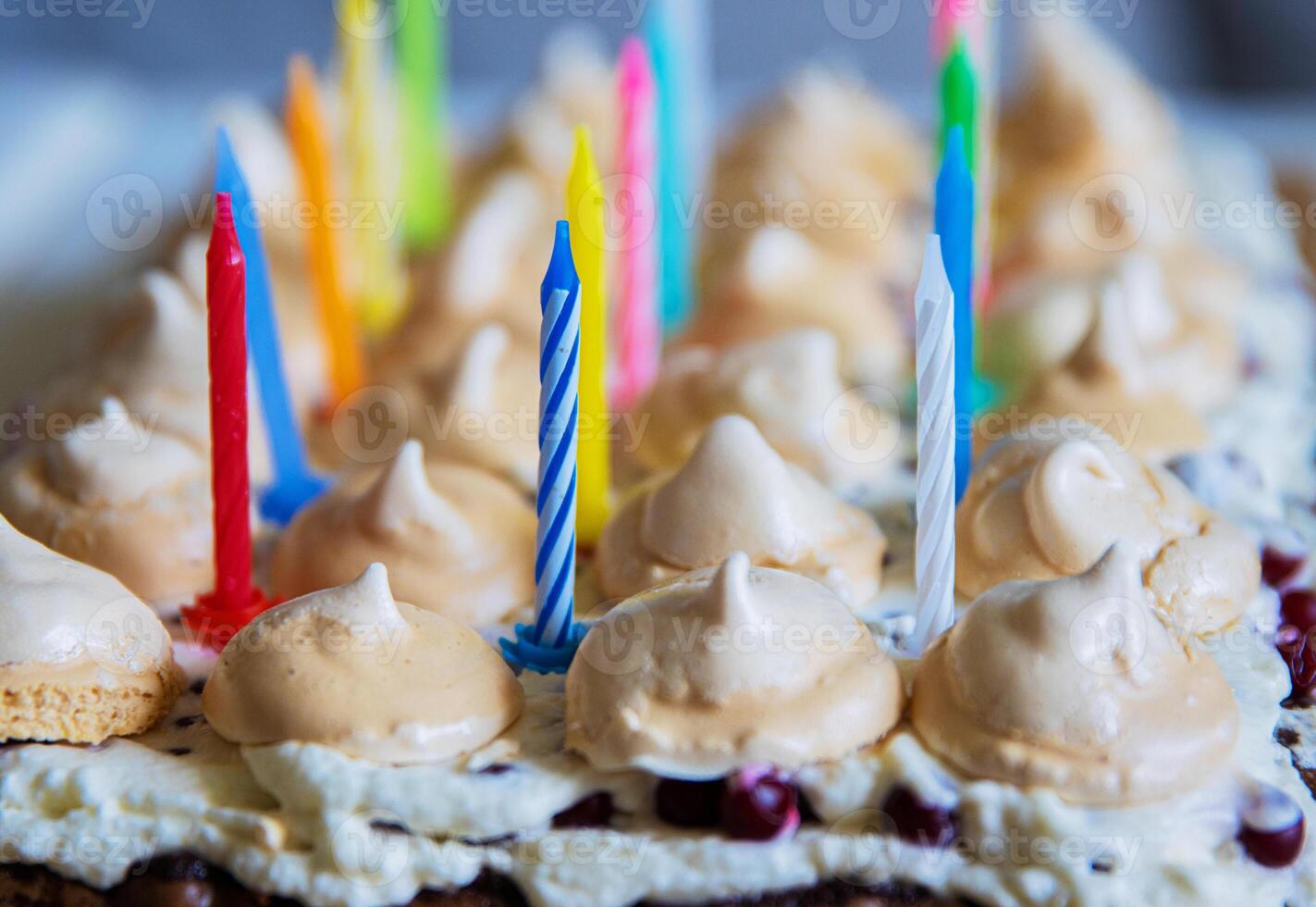 Birthday cake with white whipped cream, meringues and cranberries, decorated with multicolored lit candles. Happy Birthday concept. Tradition of making a wish blowing out candles. Selective focus. photo