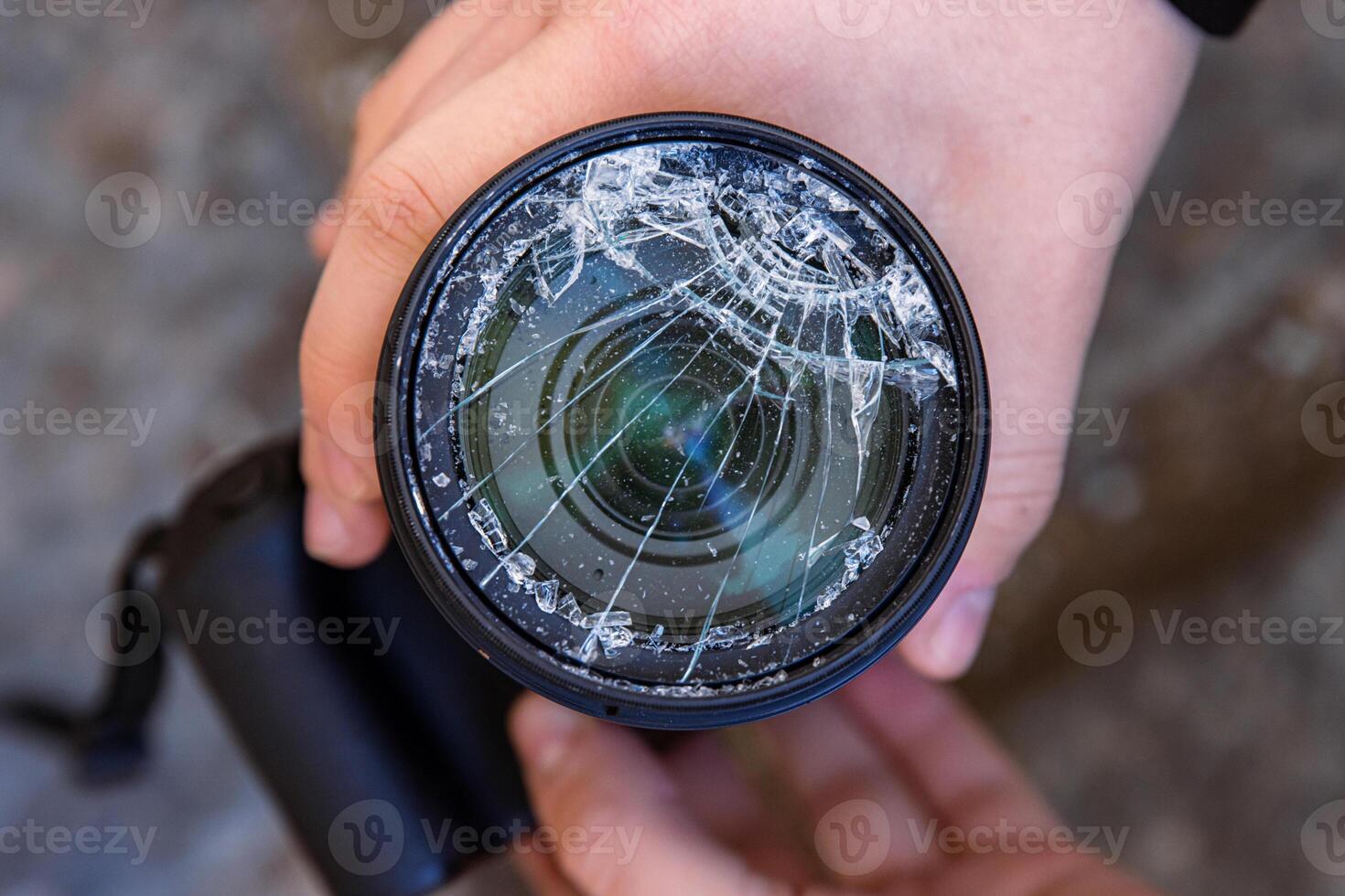 Hands of young photographer holding DSLR photo camera with broken lens filter glass after if fall down onto the floor. Close up. Destroyed cracked photo-filter. Macro. Top view. Selective focus.