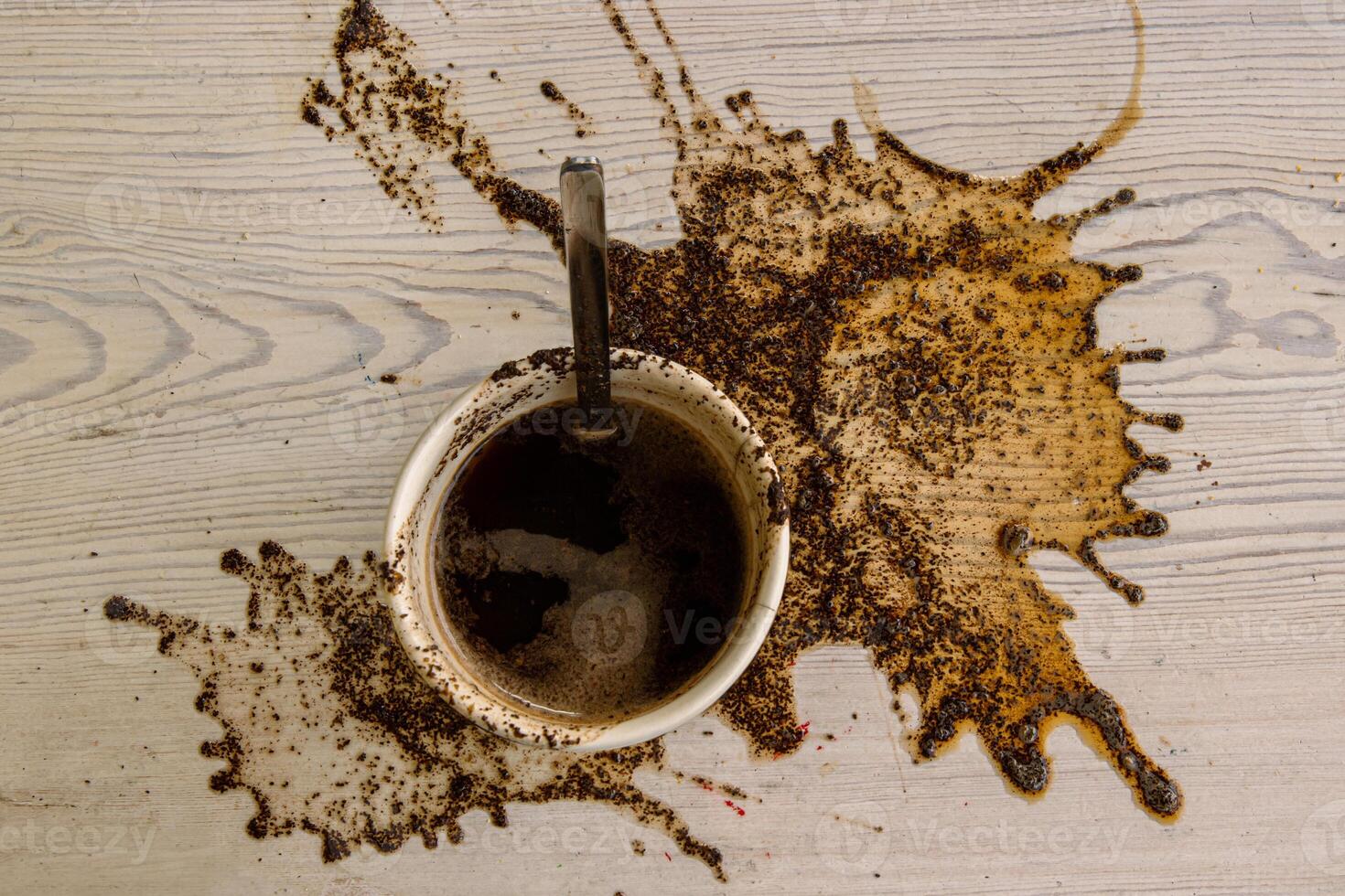 Espresso Cup with steel spoon staying on the big coffee stain. Spots of spilled coffee on white wooden texture background. Pattern, wallpaper. Top view. Closeup. Copy space. photo