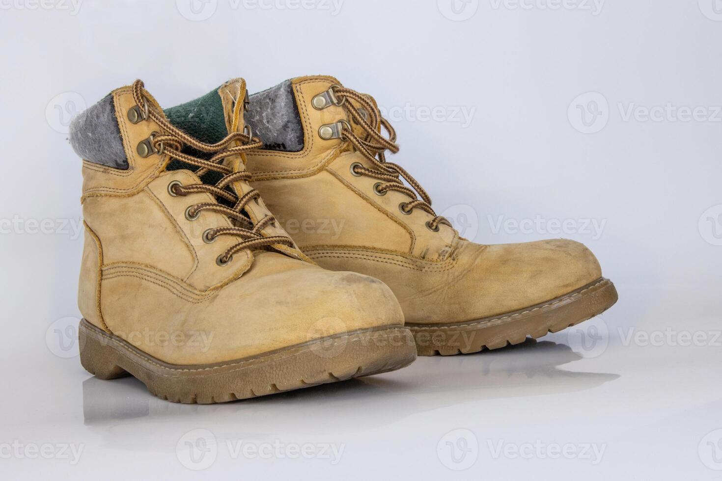 Pair of worn old yellow hiking trekking lace boots Isolated on white glossy surface with beautiful reflection effect. Second hand tourist walking shoes. Side view. Copy Space. White background. photo