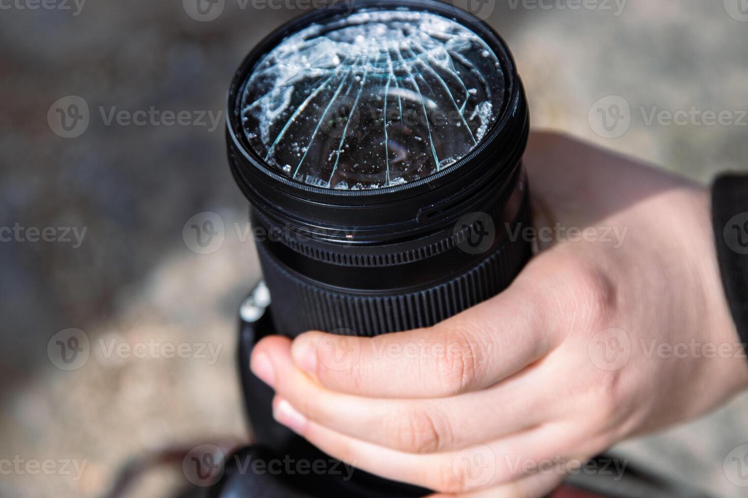 Hands of young photographer holding DSLR photo camera with broken lens filter glass after if fall down onto the floor. Close up. Destroyed cracked photo-filter. Macro. Top view. Selective focus.