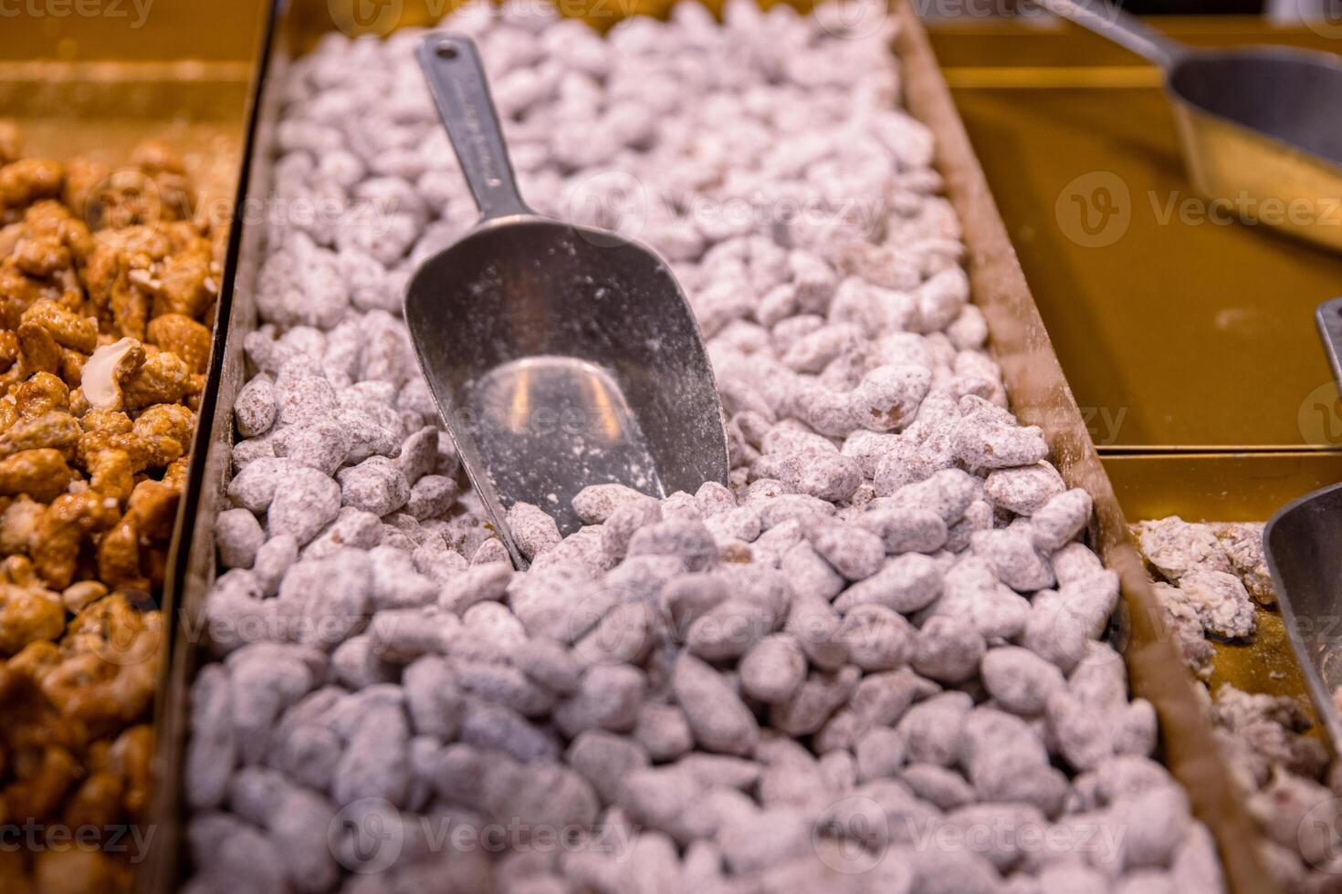 Sugared almonds. Candied sugar coated caramelized almond nuts sold on the counter at the Christmas fair market. Pile of roasted sweets on the metal tray with serving spoon. Close up Selective focus. photo