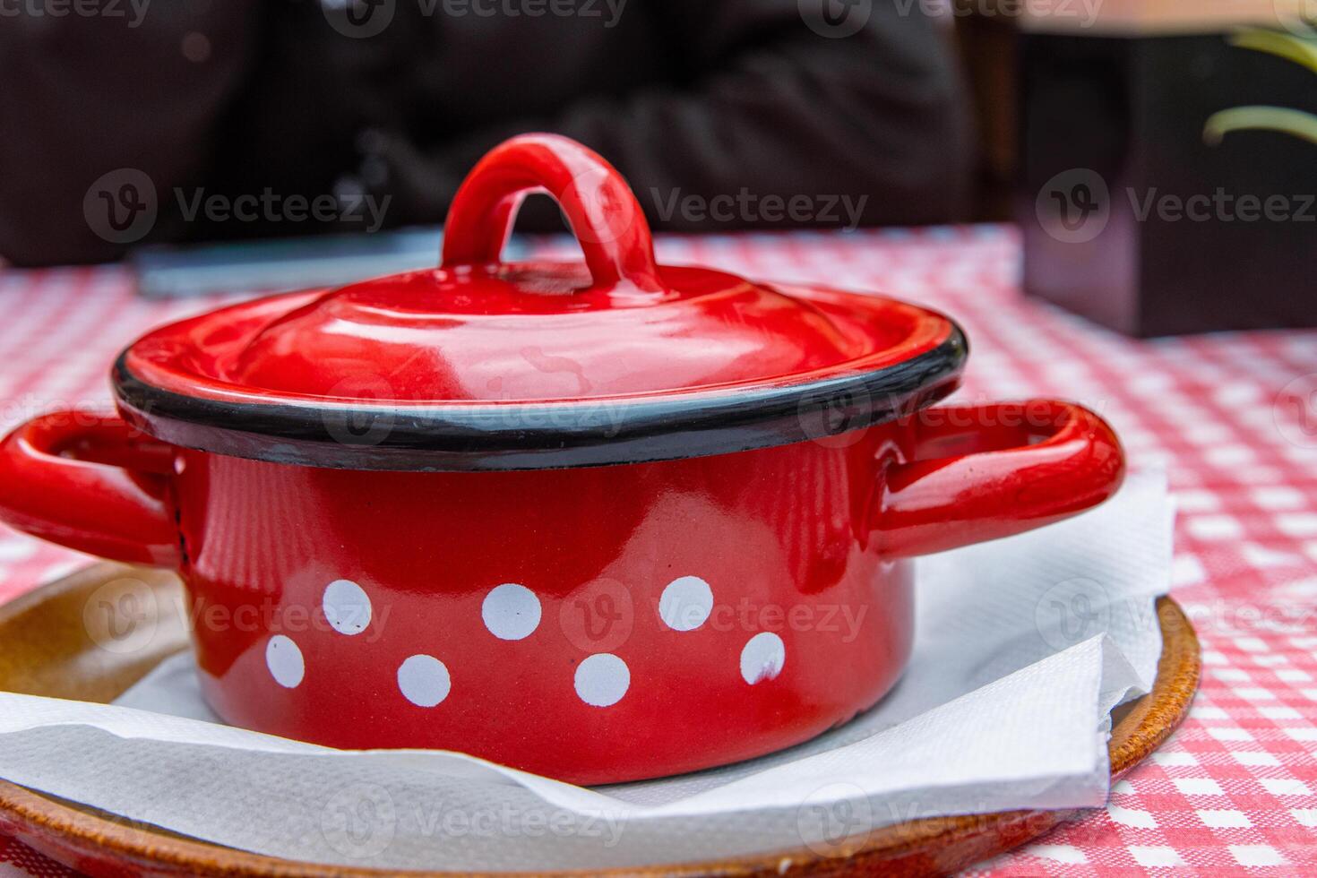 Traditional Slovak Ukrainian Russian cabbage soup with sausage and smoked meat served in retro red metal pot on the plate with spoon. Bowl of delicious Soljanka borsch with white sour cream. Top view photo
