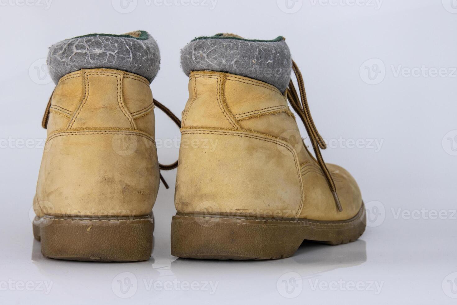 Pair of worn old yellow hiking trekking lace boots Isolated on white glossy surface with beautiful reflection effect. Second hand tourist walking shoes. Side view. Copy Space. White background. photo