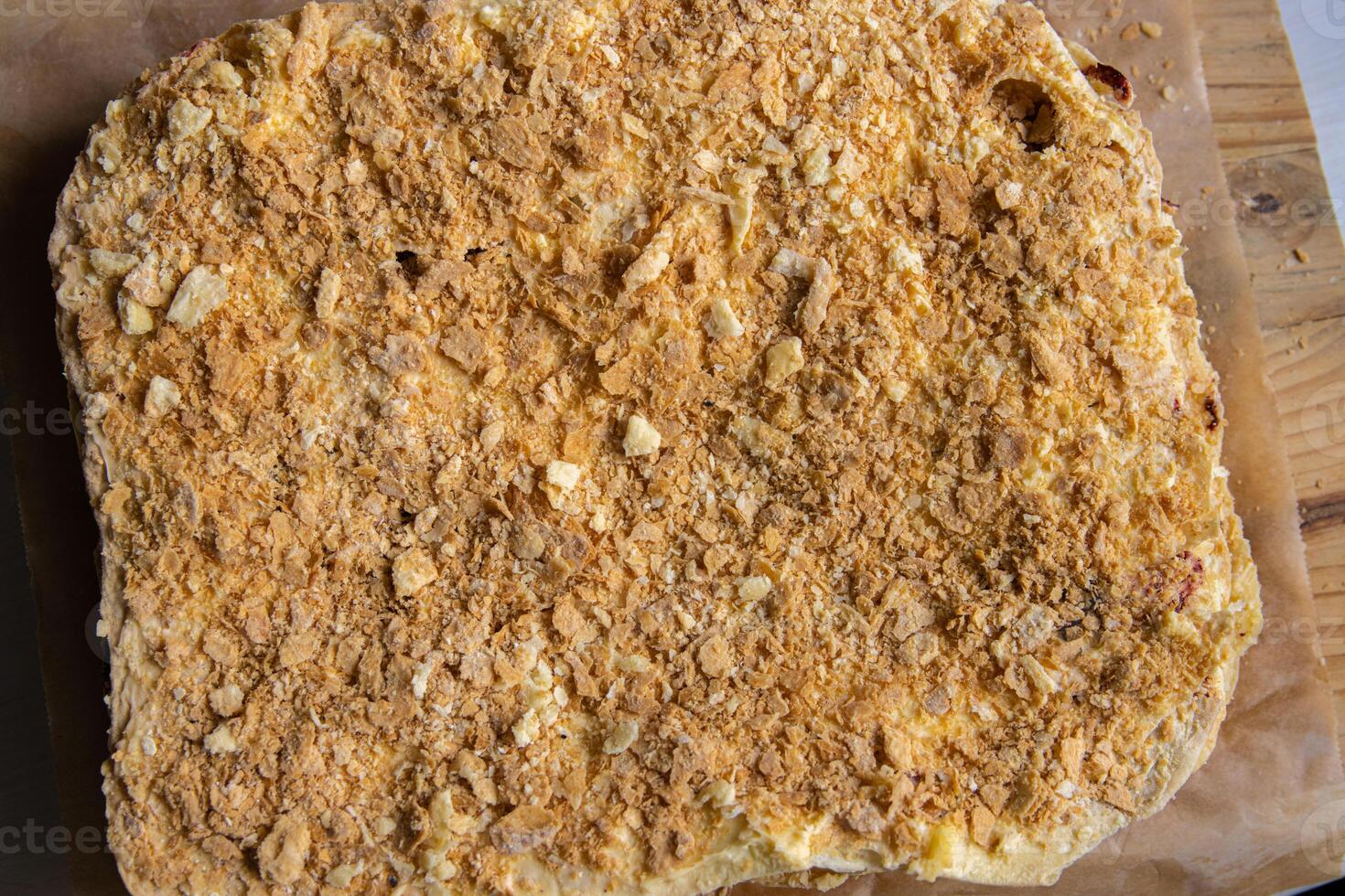 Backing process. Closeup of Puff pastry layers of the French Napoleon cake laying on the backing paper on the wooden cutting board. French pastry with custard butter cream. Top view. Selective focus. photo