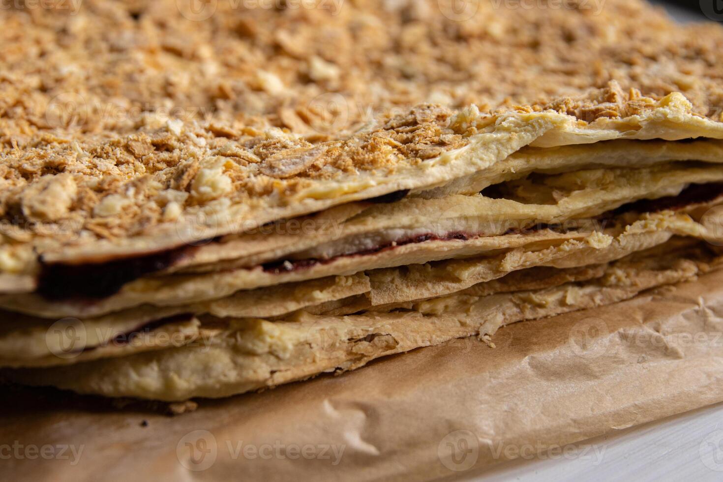 Backing process. Closeup of Puff pastry layers of the delicious French Napoleon cake laying on the backing paper. French pastry with custard butter cream. Side view. Selective focus. photo