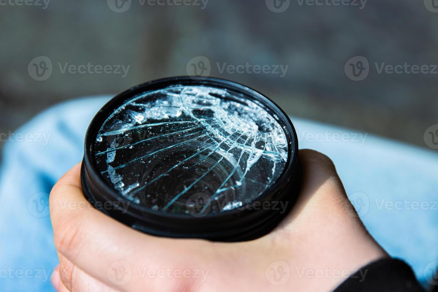 Hands of young photographer holding DSLR photo camera with broken lens filter glass after if fall down onto the floor. Close up. Destroyed cracked photo-filter. Macro. Top view. Selective focus.