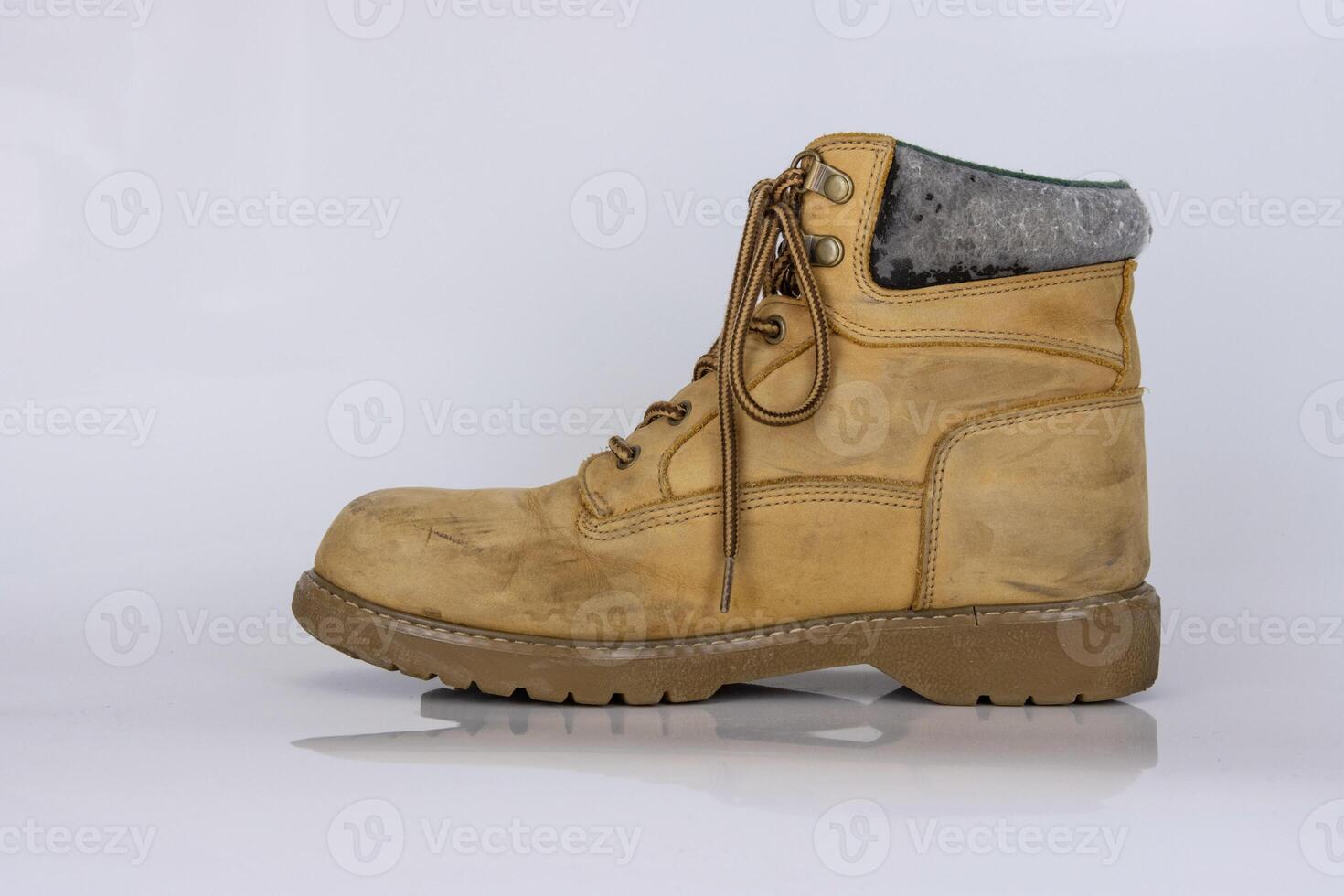 One worn old yellow hiking trekking lace boots Isolated on white glossy surface with beautiful reflection effect. Second hand tourist walking shoes. Side view. Copy Space. White background. photo