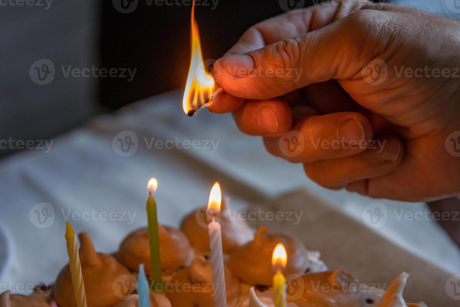 Mens Hand holding matches and lighting colorful candles on the large homemade chocolate birthday cake, decorated with meringues and whipped cream. Close-up. Selective focus. photo