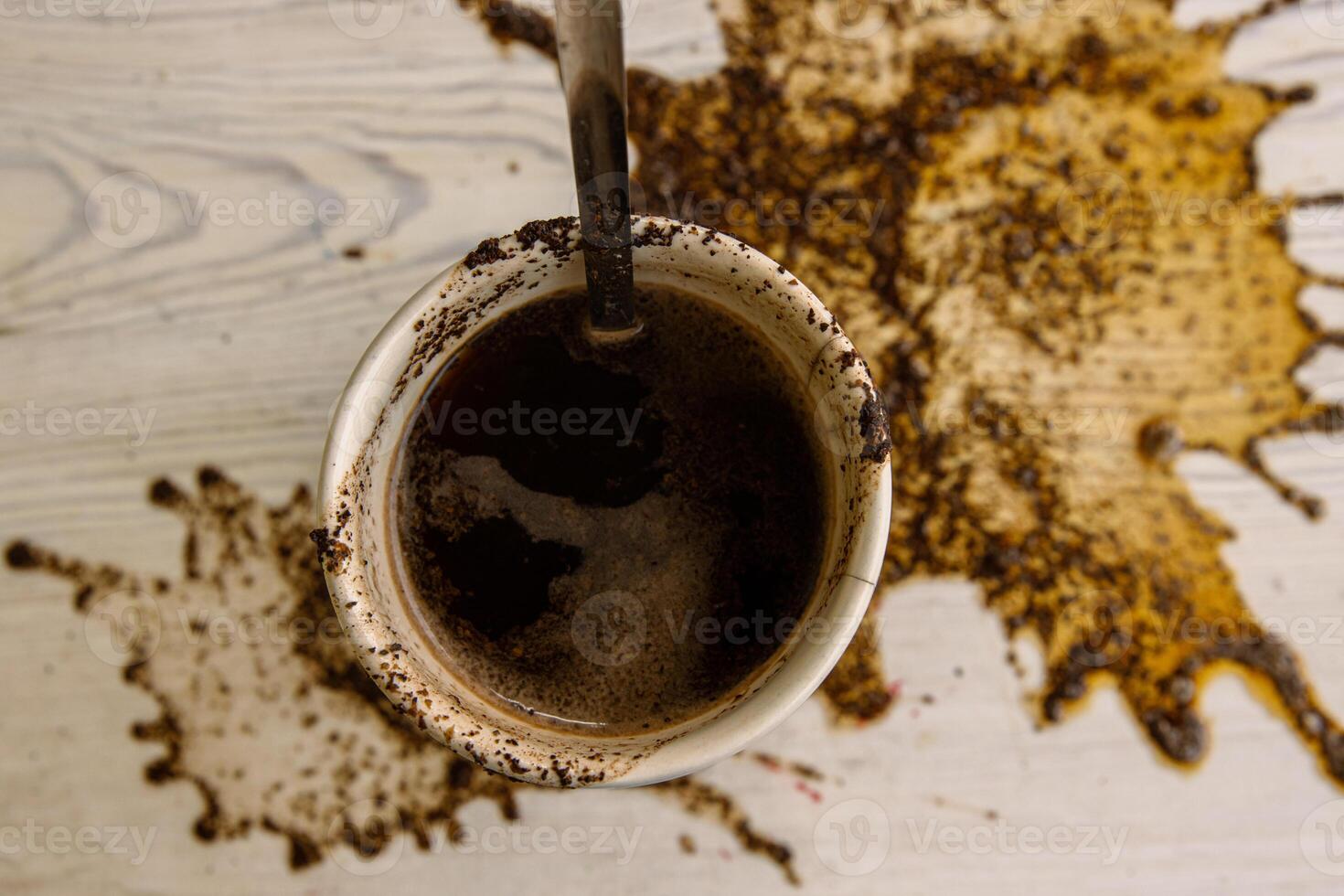 Espresso Cup with steel spoon staying on the big coffee stain. Spots of spilled coffee on white wooden texture background. Pattern, wallpaper. Top view. Closeup. Copy space. photo