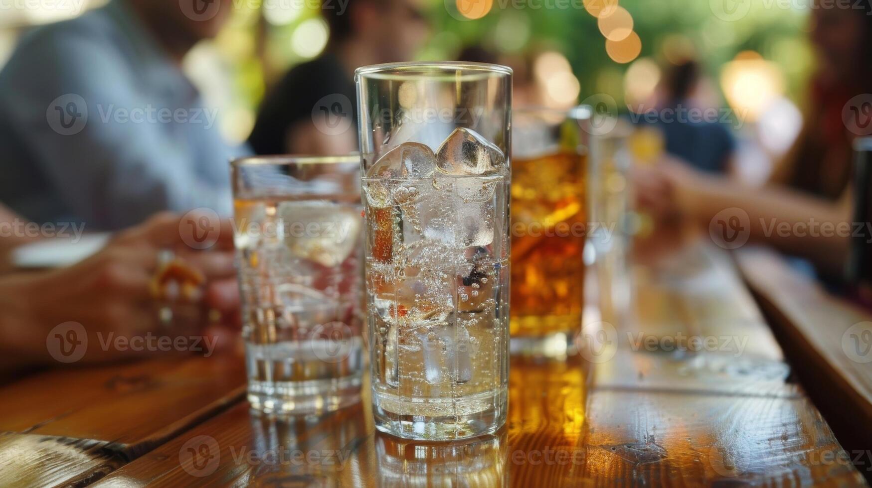 A group of friends sits at a long wooden table each holding a small glass of carbonated liquid in front of them photo