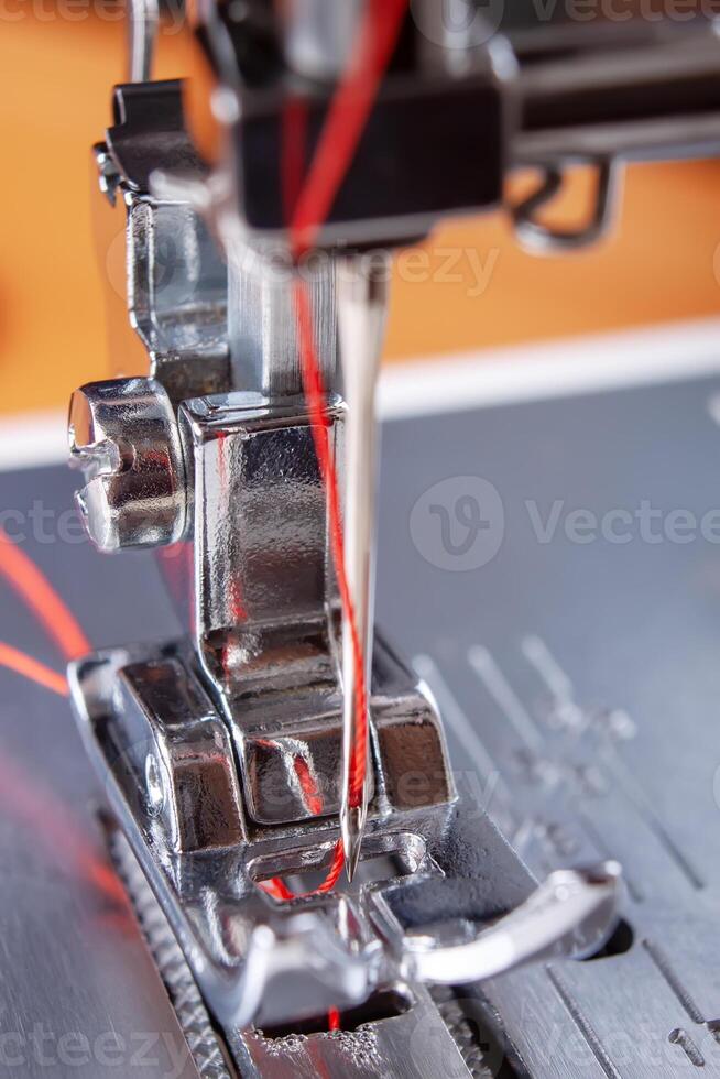 Modern sewing machine presser foot with red thread close up photo