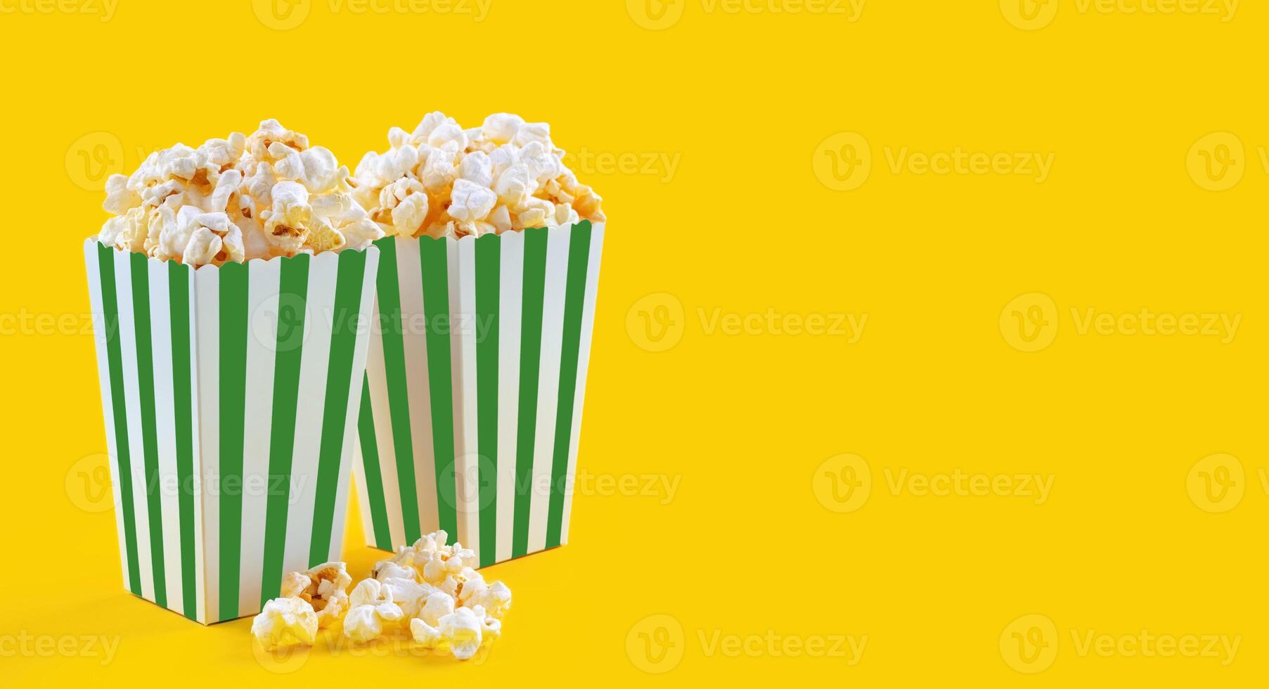 Green white striped carton bucket with tasty cheese popcorn, isolated on yellow background photo