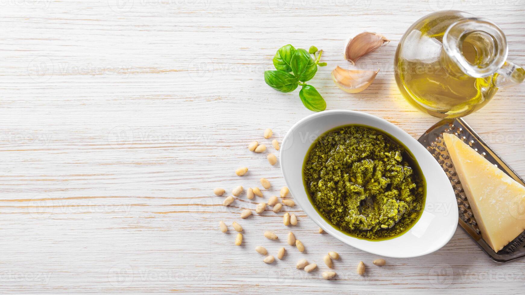 hecho en casa pesto salsa en pequeño redondo blanco tarro y ingredientes en blanco de madera antecedentes foto