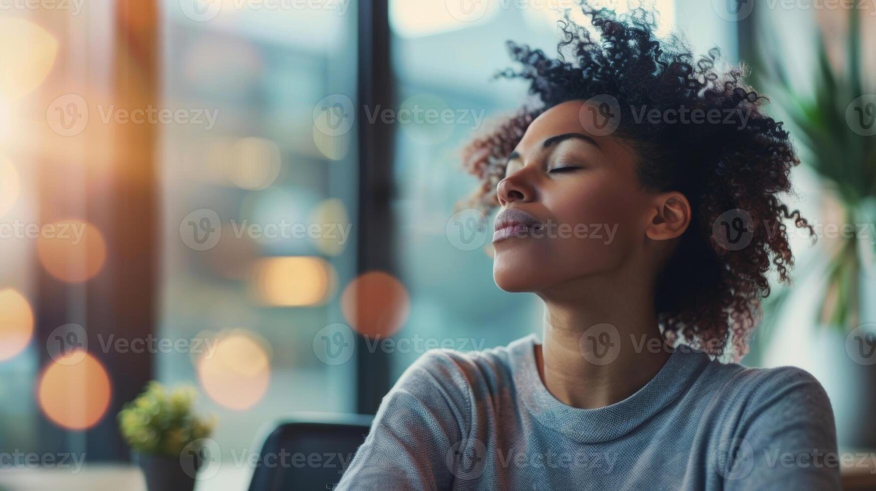 A person sits at their desk with their eyes closed taking a break from work to refocus and engage in mindful breathing photo