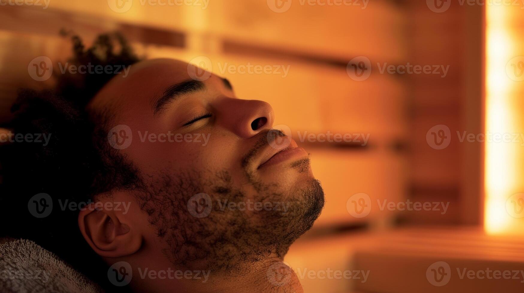 A person with their head tilted back eyes closed and a serene smile while listening to a guided relaxation audio in the sauna. photo