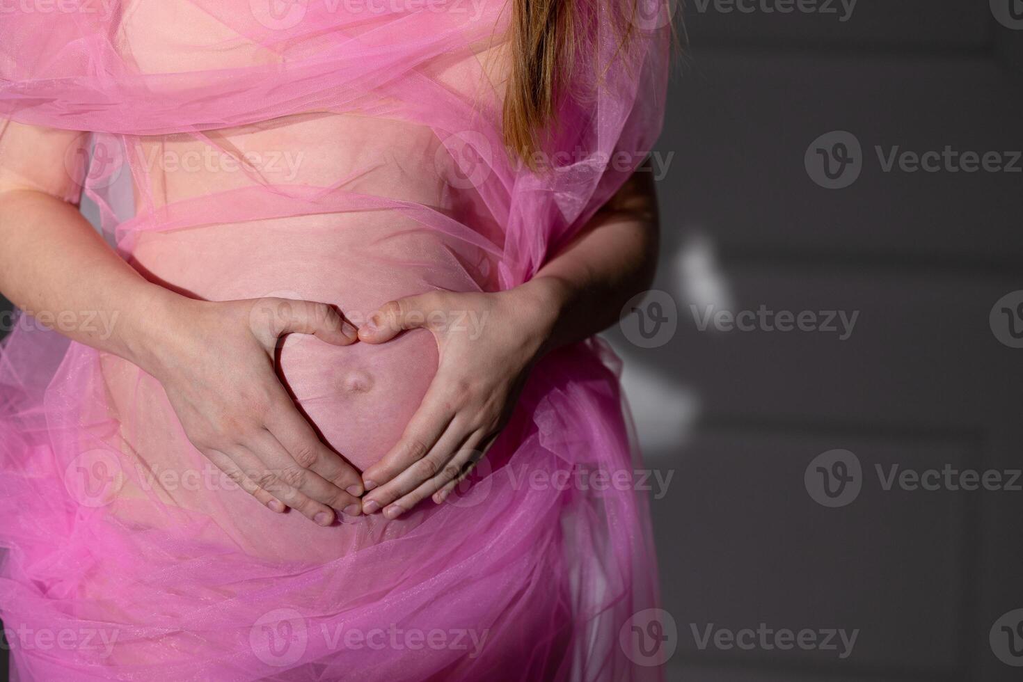 Close-up belly pregnant pink transparent fabric fingers folded like heart stomach concept happy motherhood preparation photo