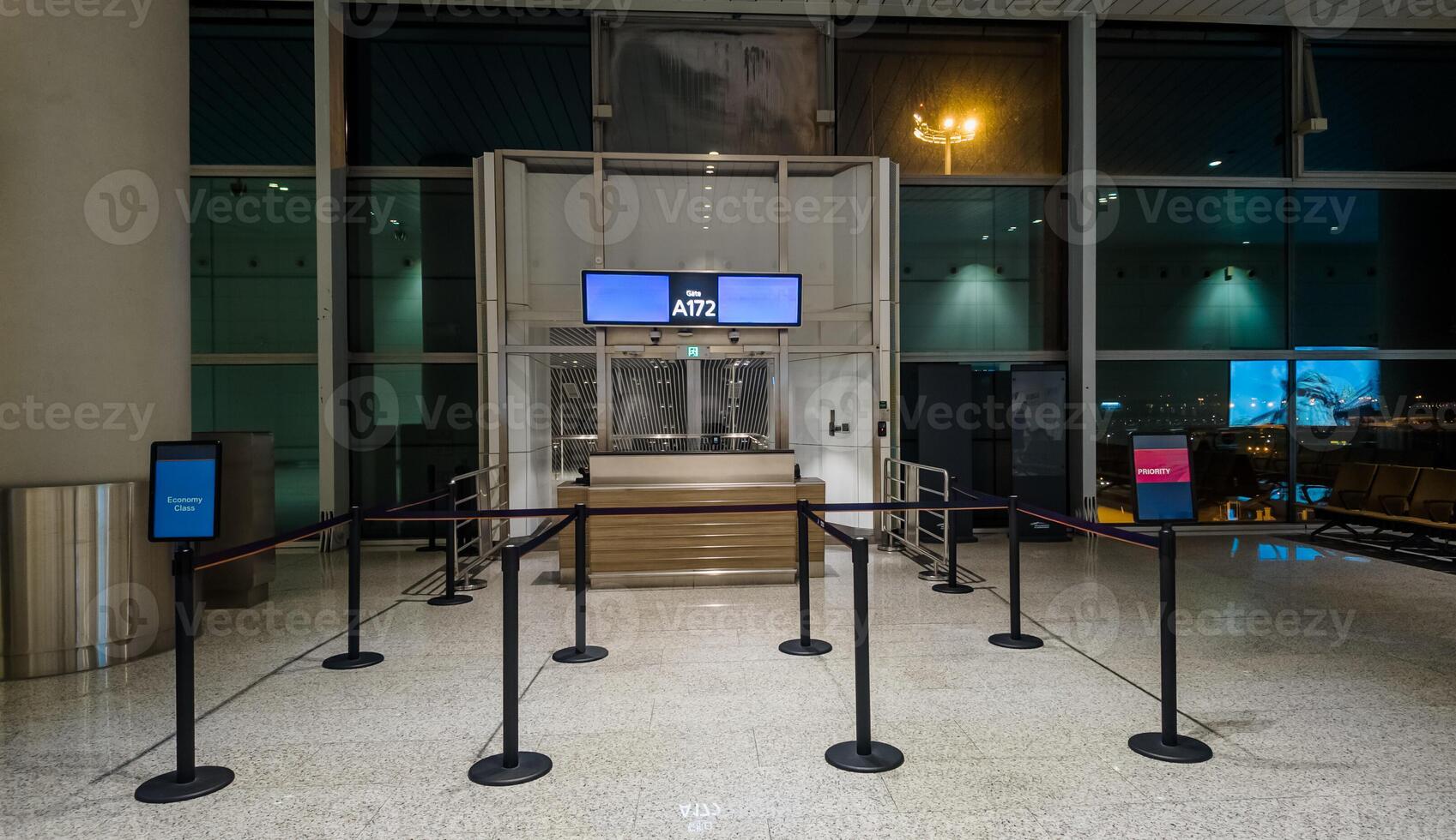 Empty airport gate with stanchion barriers at night, suggesting concepts of travel, business trips, and less crowded off peak holiday times photo