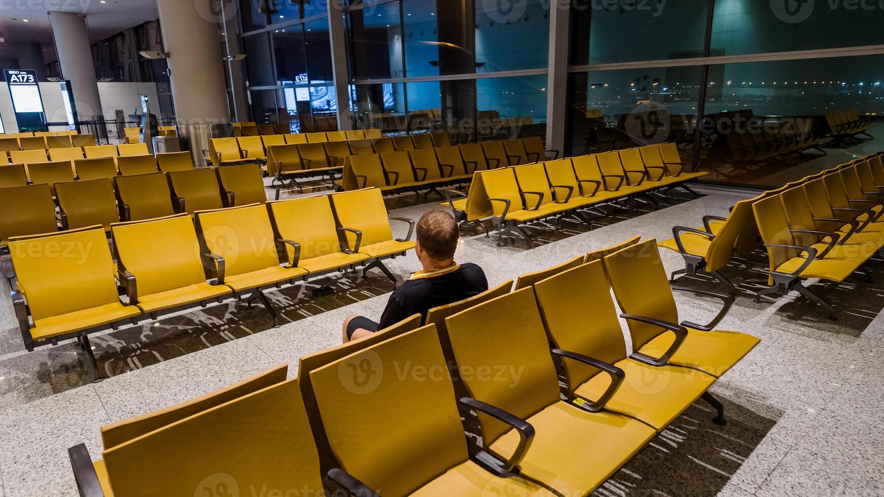 Lone traveler sitting in an empty airport waiting area with rows of yellow seats, suggesting travel, business trips, or holiday commuting photo