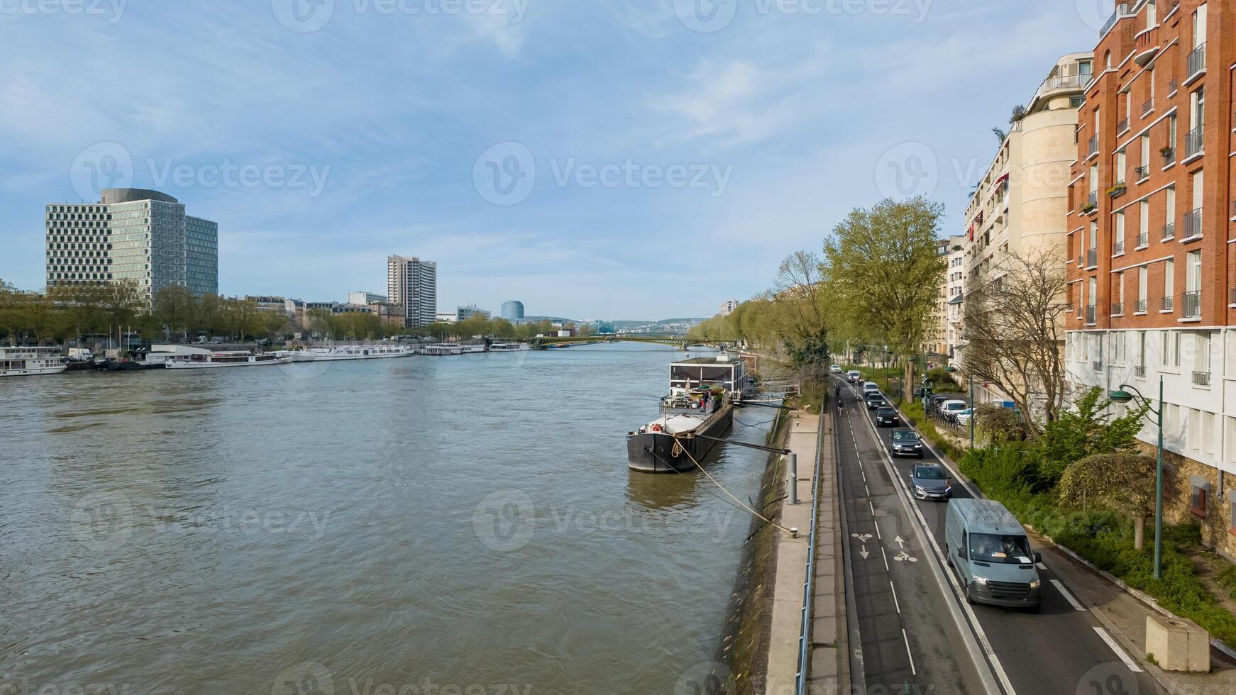 Panoramic view of urban riverfront with moored boats, promenade, and modern architecture on a clear day, ideal for travel and urban planning concepts photo