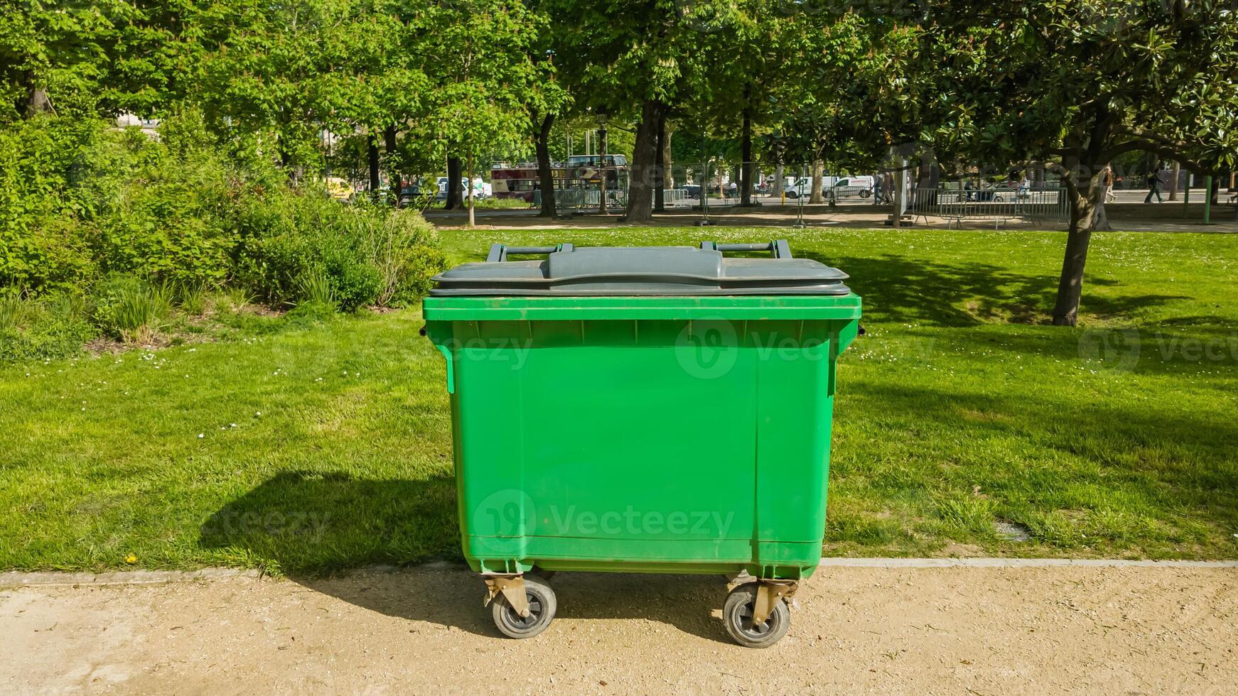 Bright green waste container in a sunlit urban park setting, symbolizing environmental conservation and cleanliness, suitable for Earth Day and public service campaigns photo