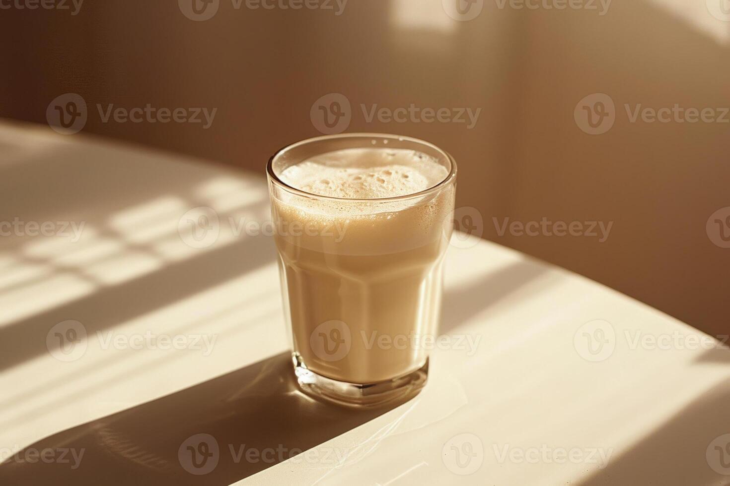 Glass of frothy milk on a table, soft light casting a shadow against a beige to white gradient background photo