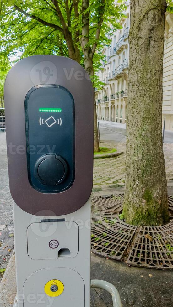 Modern electric vehicle charging station on a city street with lush green trees, signifying sustainable transportation and environmental awareness photo