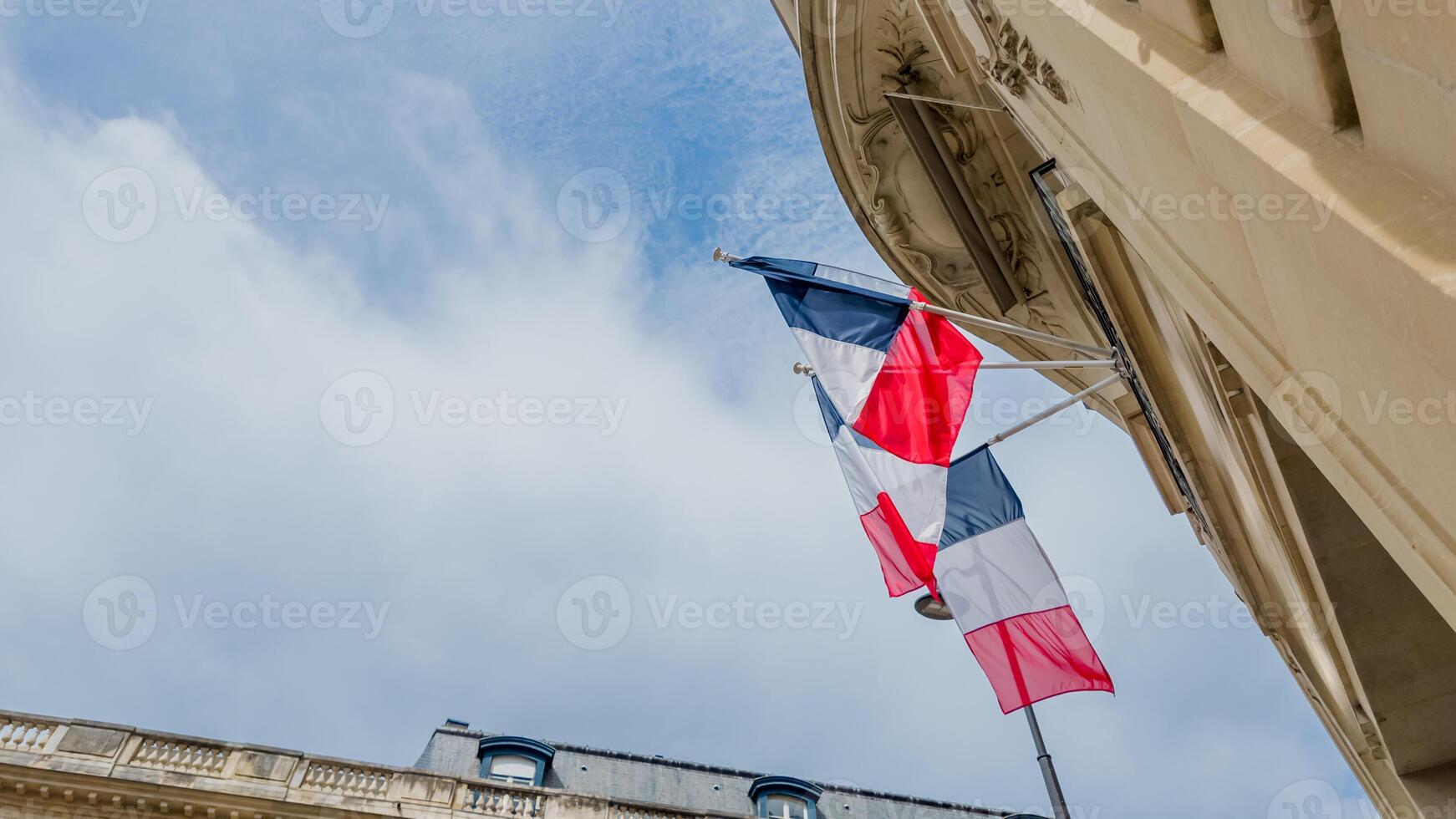 French tricolor flag waving against a clear blue sky, symbolizing Bastille Day and national pride, attached to classic European architecture photo