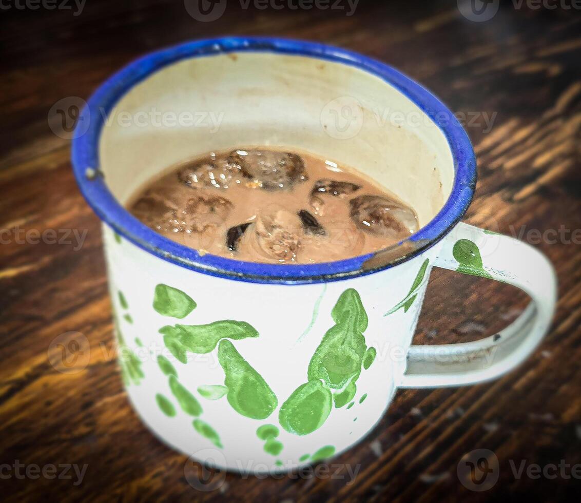 Ice chocolate drink on a vintage Indonesian iron mug with random green pattern called Blirik cup or cangkir Blirik on bokeh background along with chocolate filling bread photo
