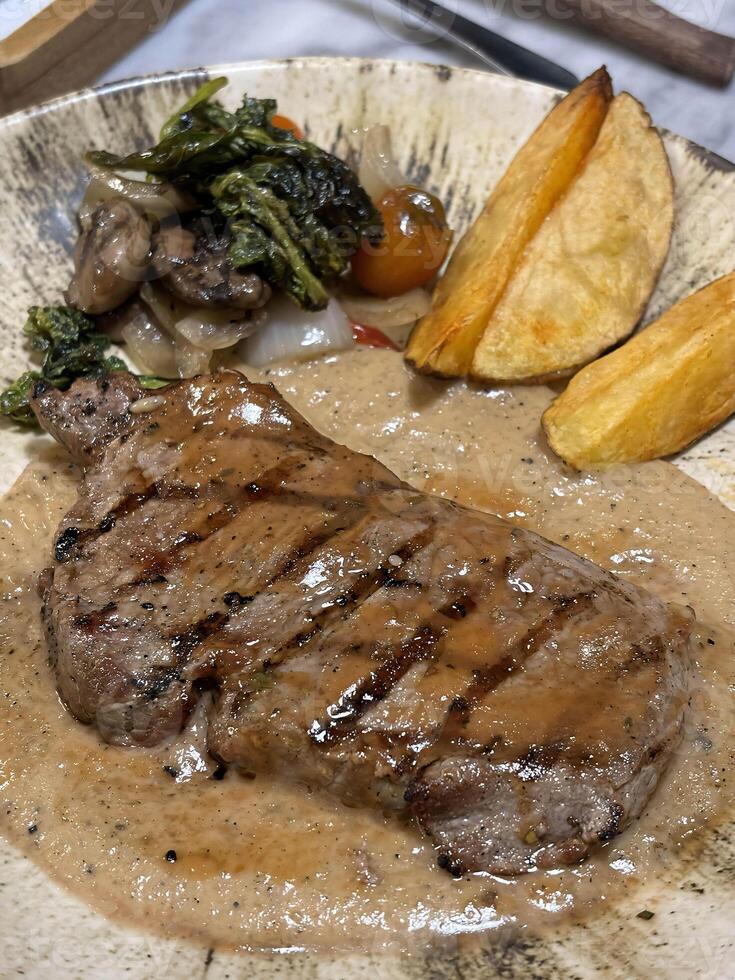 Sirloin steak grilled medium rare served with potatoes and salad with mushroom black pepper sauce in a restaurant photo