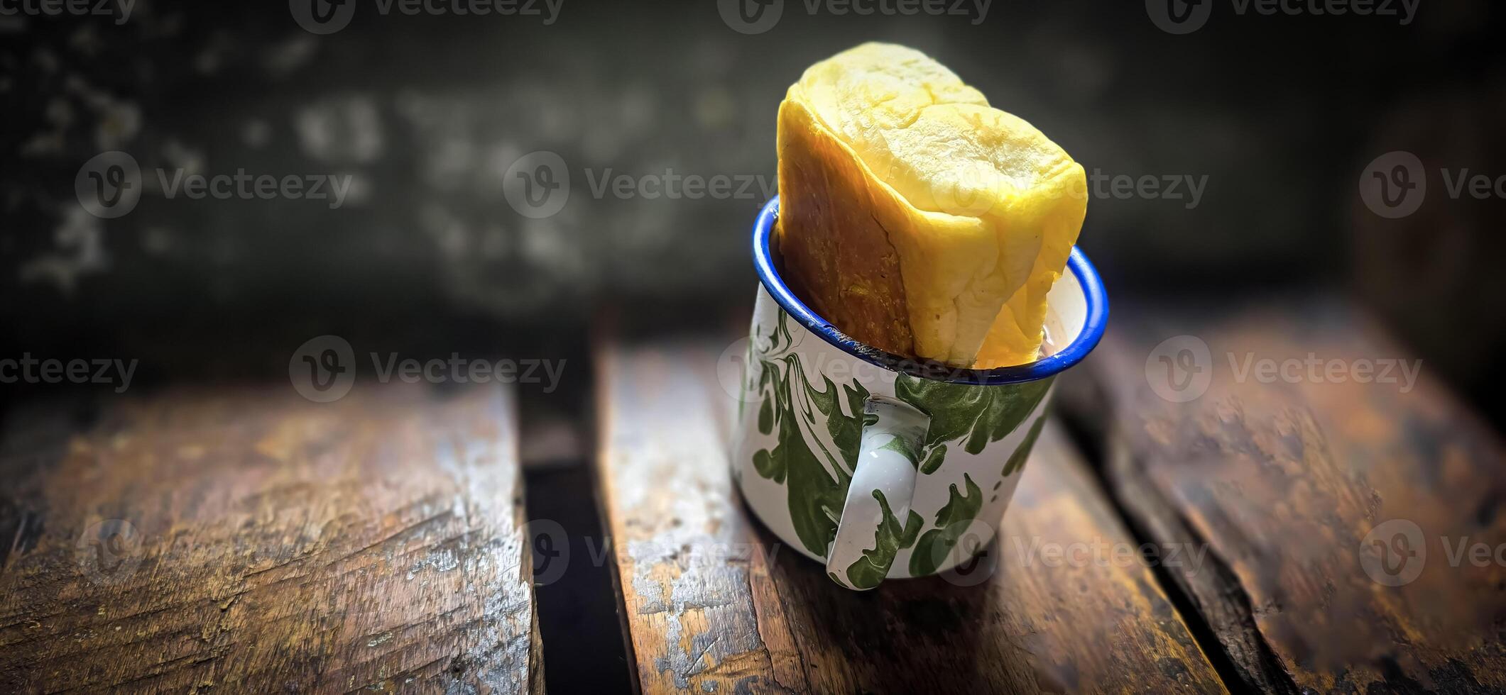 Ice chocolate drink on a vintage Indonesian iron mug with random green pattern called Blirik cup or cangkir Blirik on bokeh background along with chocolate filling bread photo