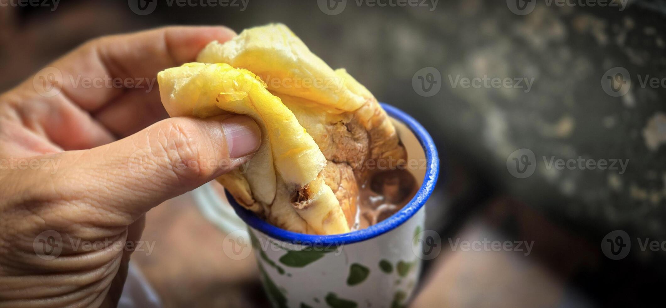 Ice chocolate drink on a vintage Indonesian iron mug with random green pattern called Blirik cup or cangkir Blirik on bokeh background along with chocolate filling bread photo