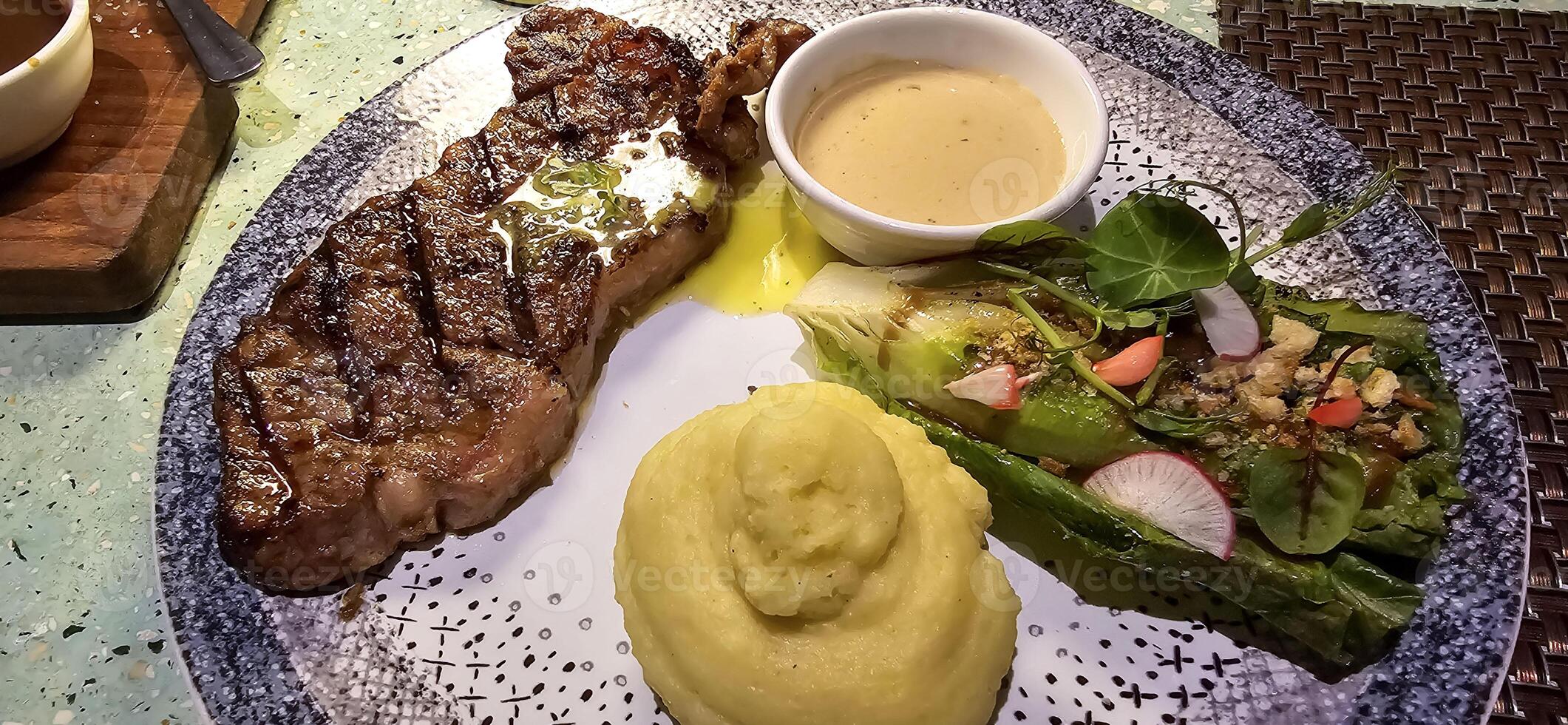 Beef New York strip loin steak or sirloin steak served with potatoes, and mushroom sauce and salad on plate photo