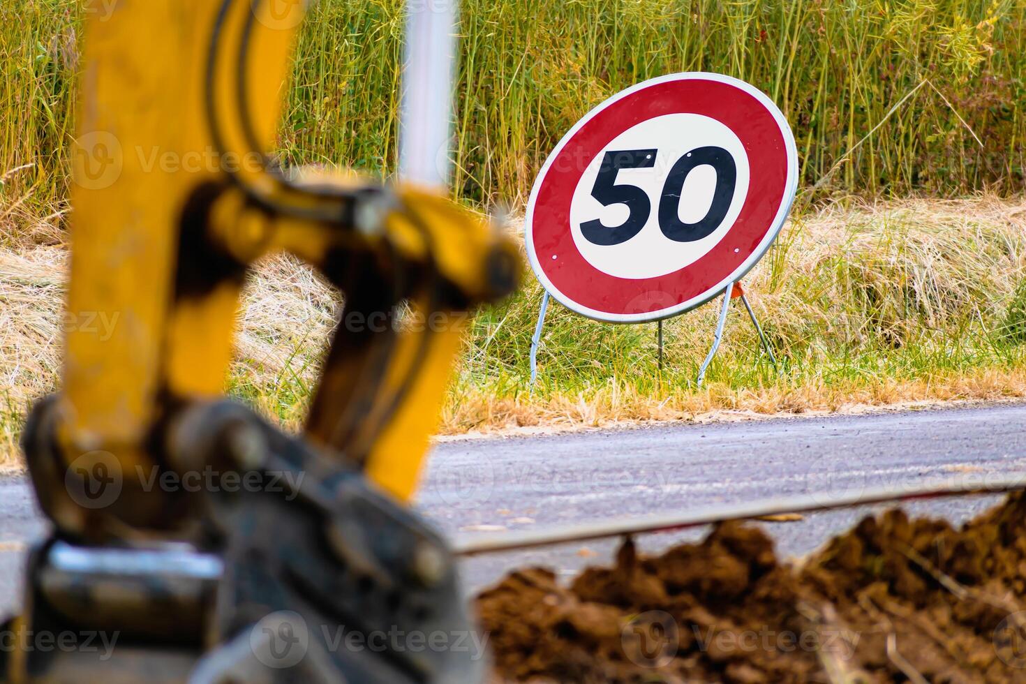 Arm of a mini digger and bucket with a speed limit sign at 50, road sign photo