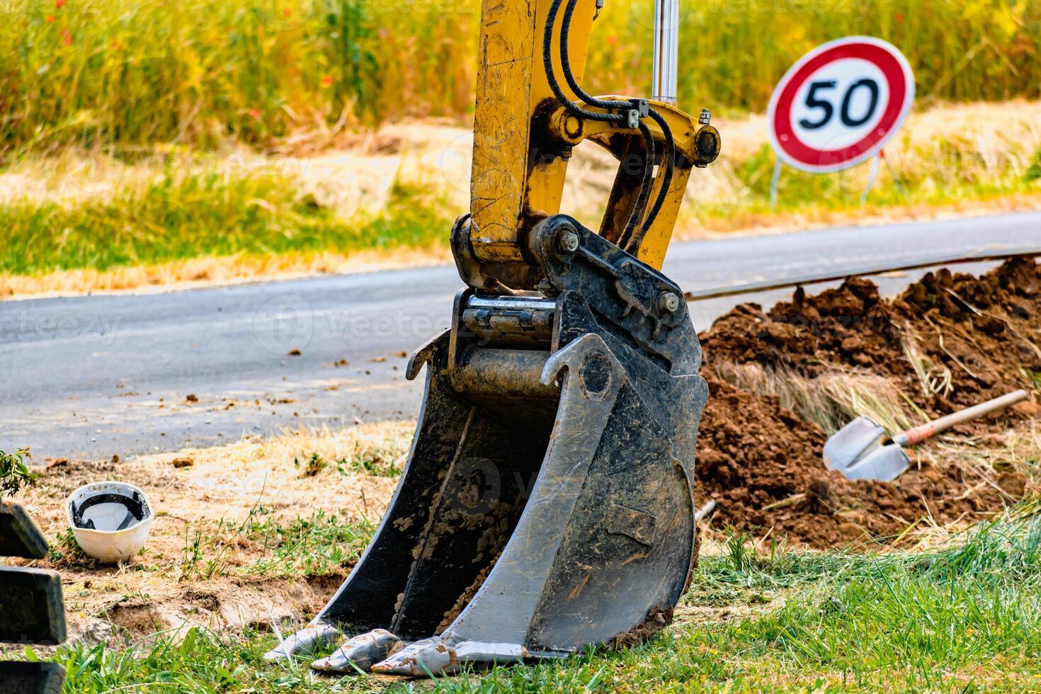 Arm of a mini digger and bucket with a speed limit sign at 50, road sign photo