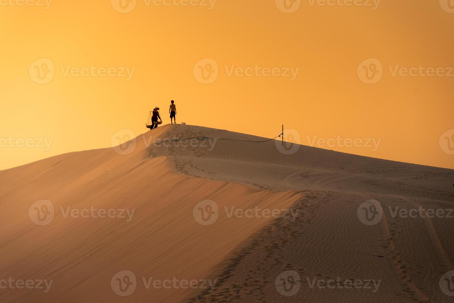 Aerial view of a peasant woman carries a bamboo frame on the shoulder across sand dunes in Ninh Thuan province, Vietnam. It is one of the most beautiful places in Vietnam photo