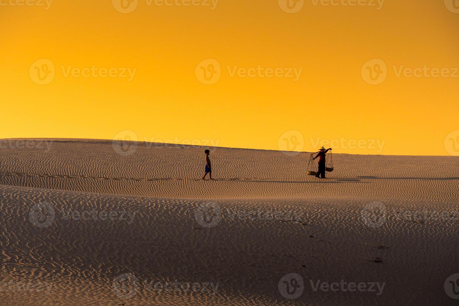 Aerial view of a peasant woman carries a bamboo frame on the shoulder across sand dunes in Ninh Thuan province, Vietnam. It is one of the most beautiful places in Vietnam photo