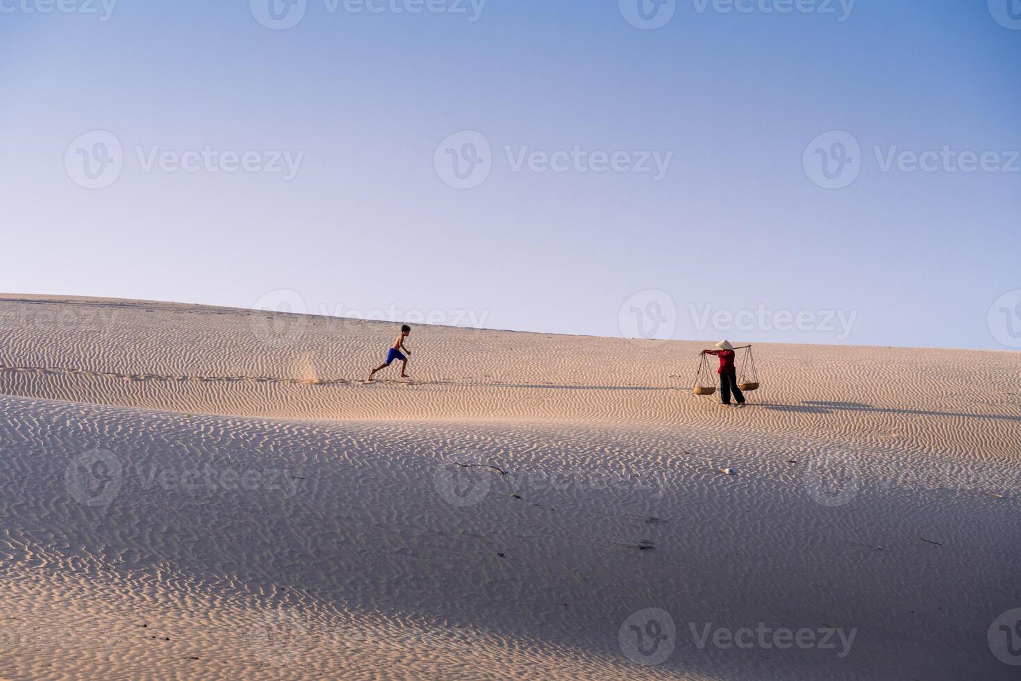 Aerial view of a peasant woman carries a bamboo frame on the shoulder across sand dunes in Ninh Thuan province, Vietnam. It is one of the most beautiful places in Vietnam photo