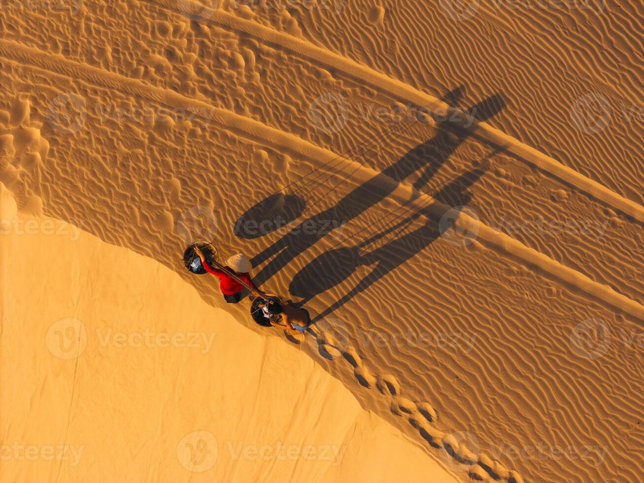 Aerial view of a peasant woman carries a bamboo frame on the shoulder across sand dunes in Ninh Thuan province, Vietnam. It is one of the most beautiful places in Vietnam photo