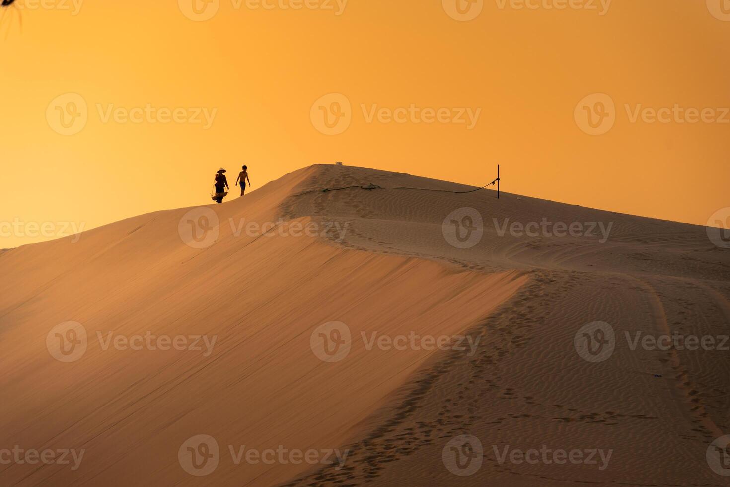 Aerial view of a peasant woman carries a bamboo frame on the shoulder across sand dunes in Ninh Thuan province, Vietnam. It is one of the most beautiful places in Vietnam photo