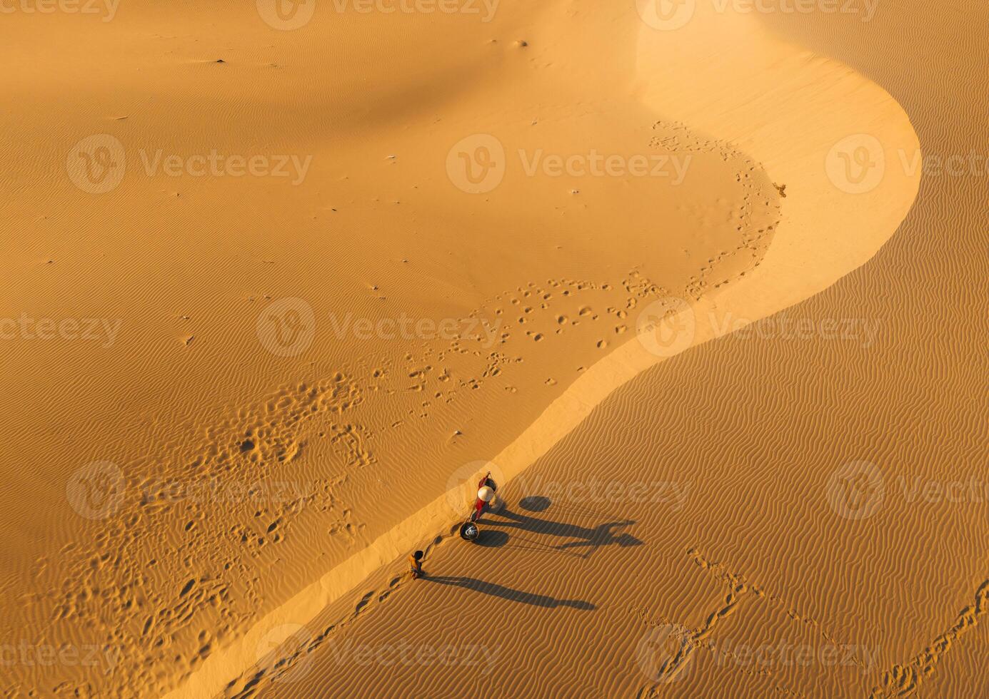 Aerial view of a peasant woman carries a bamboo frame on the shoulder across sand dunes in Ninh Thuan province, Vietnam. It is one of the most beautiful places in Vietnam photo